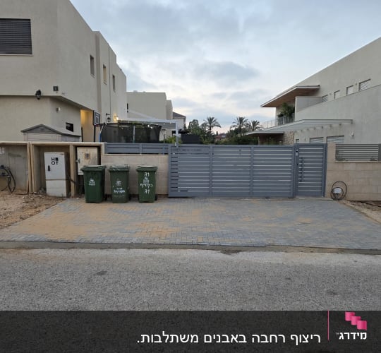 חצר עם שער וגדר, פחי אשפה ובתים ברקע